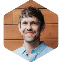 Alan, smiling at the camera and wearing a blue button up over a wooden background