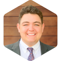 CJ smiling with a suit and tie on a wooden background.